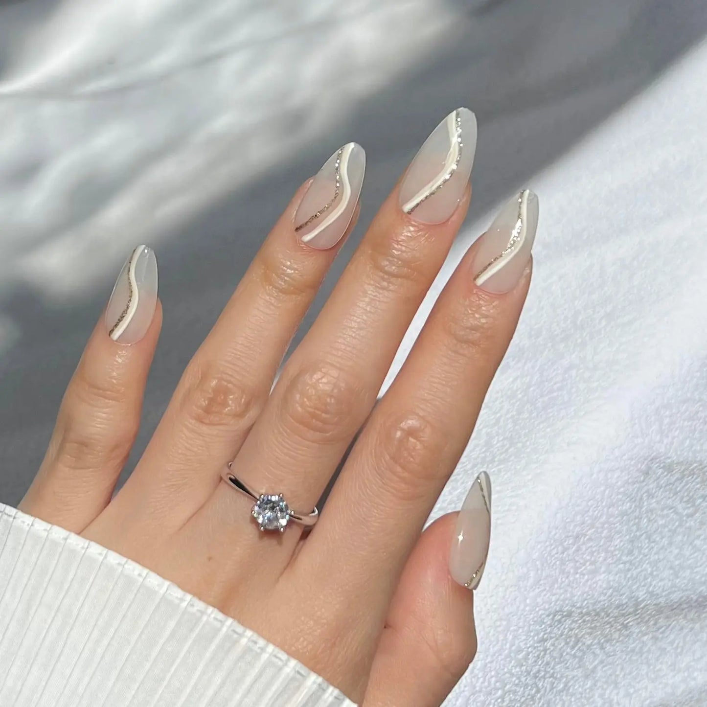 A hand showcasing nude press-on nails with fine metallic lines, offering a refined and glamorous appearance.