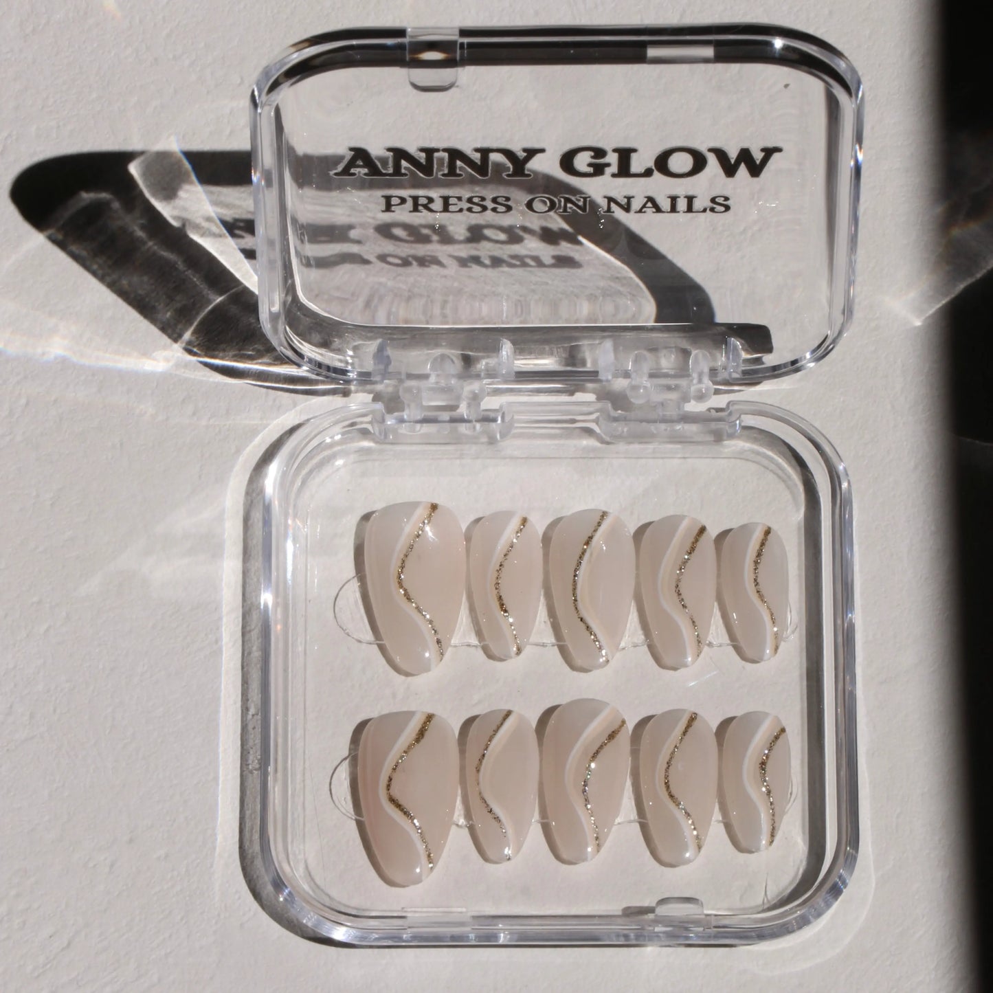 A set of press-on nails displayed in a clear plastic box, featuring a nude base with delicate metallic line accents for a modern, elegant look.