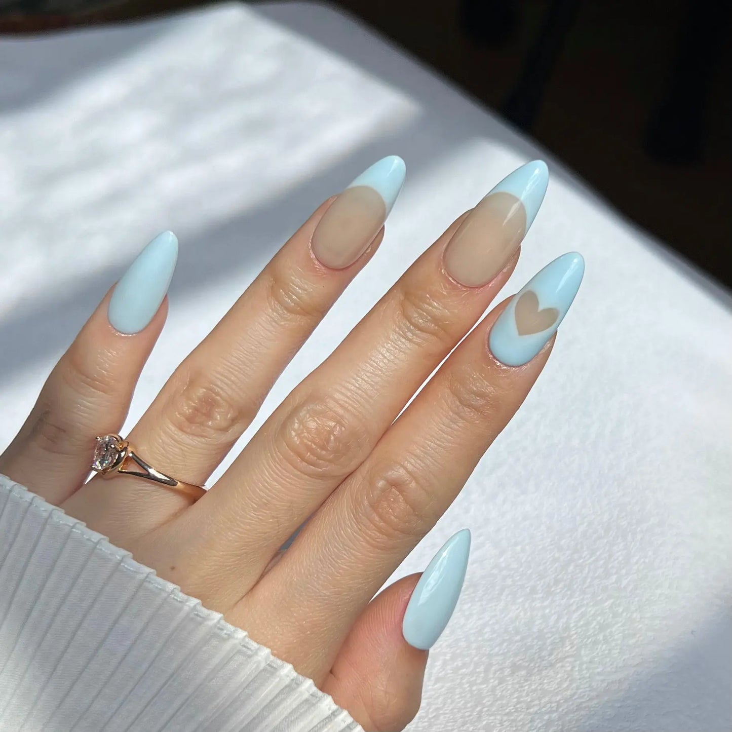 A hand showcasing pastel blue press-on nails with a translucent nude base, perfect for a chic and modern style.