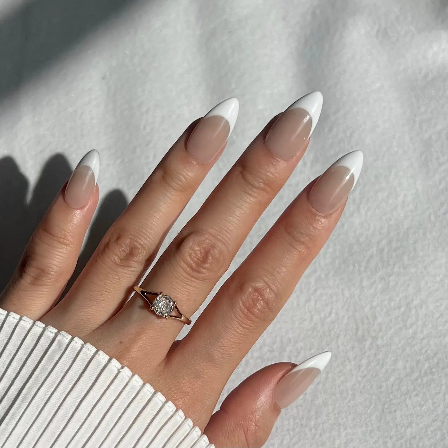 A hand showcasing French-tipped press-on nails with bold white tips and a nude base, perfect for a refined and modern style.