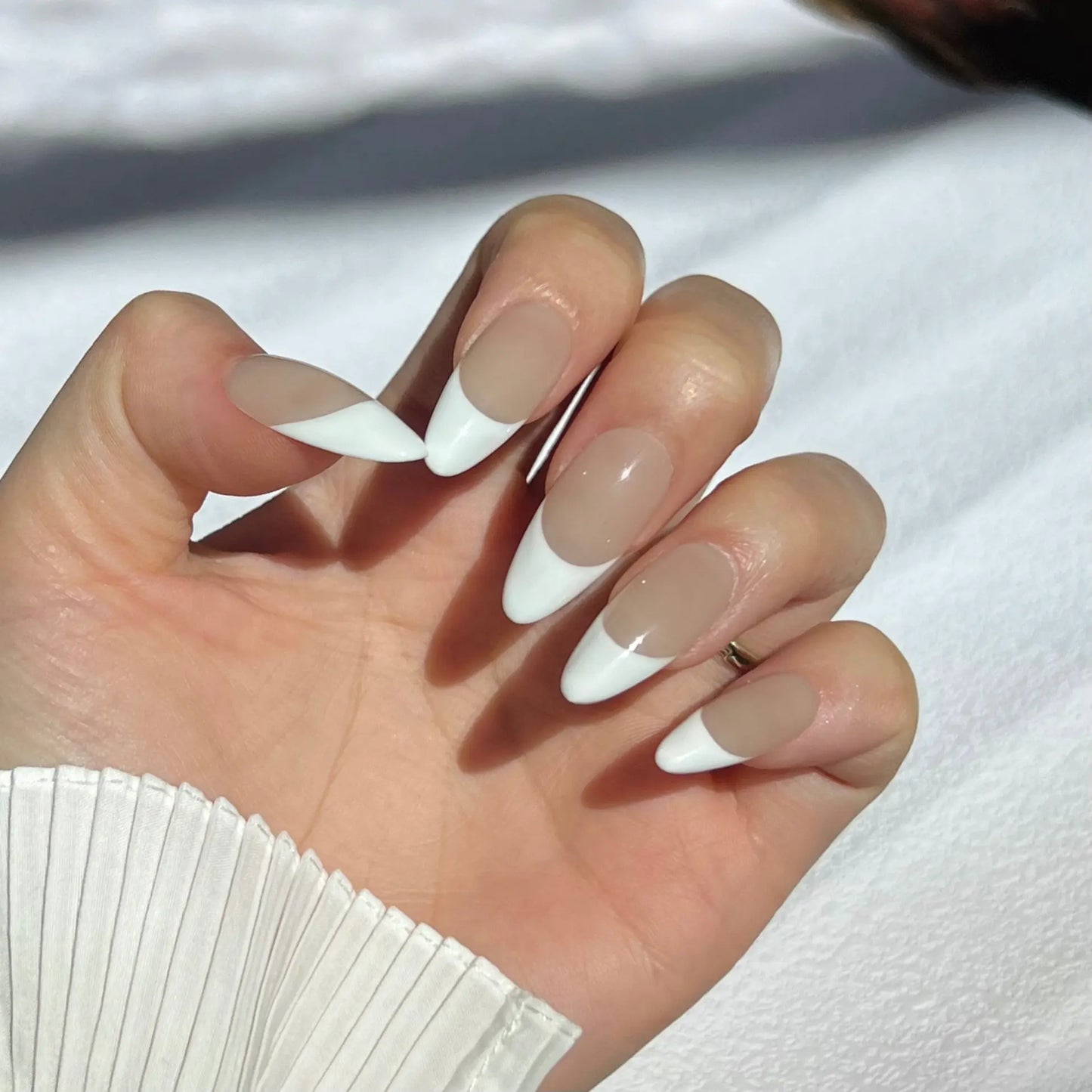 A close-up of a hand wearing almond-shaped press-on nails with a nude base and crisp white French tips, offering a timeless and sophisticated look.