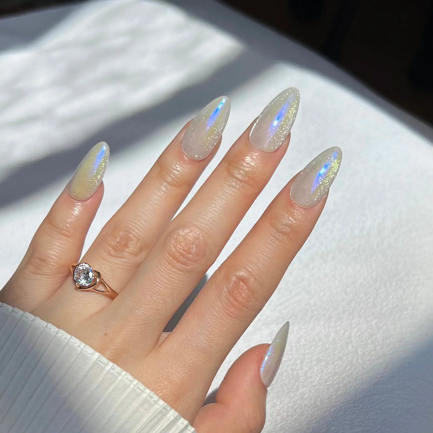 A set of press-on nails in a clear plastic box featuring a shimmery, iridescent finish inspired by the Northern Lights, with a delicate holographic glow.