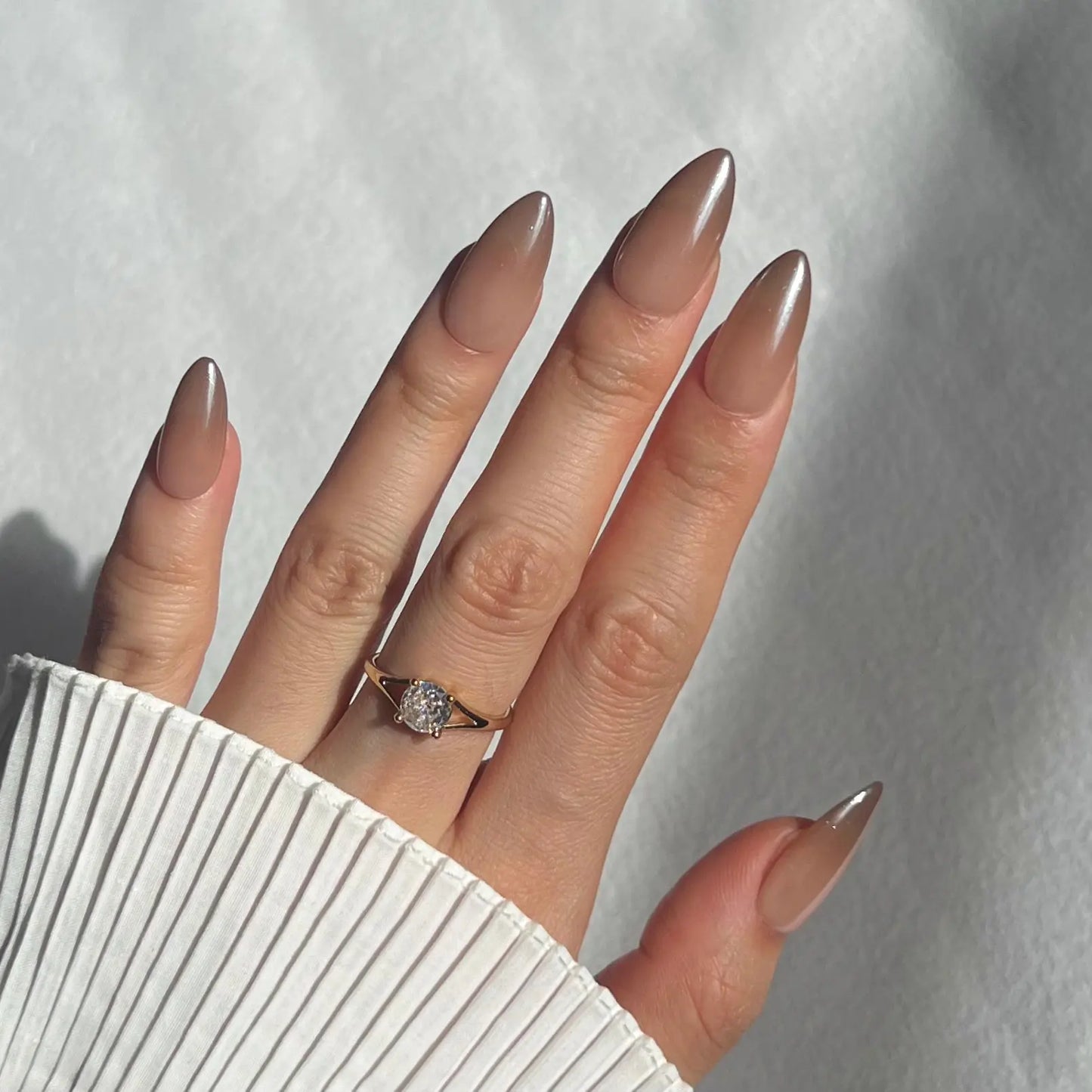  A hand showcasing translucent beige press-on nails with a high-gloss finish, offering a subtle and refined look.