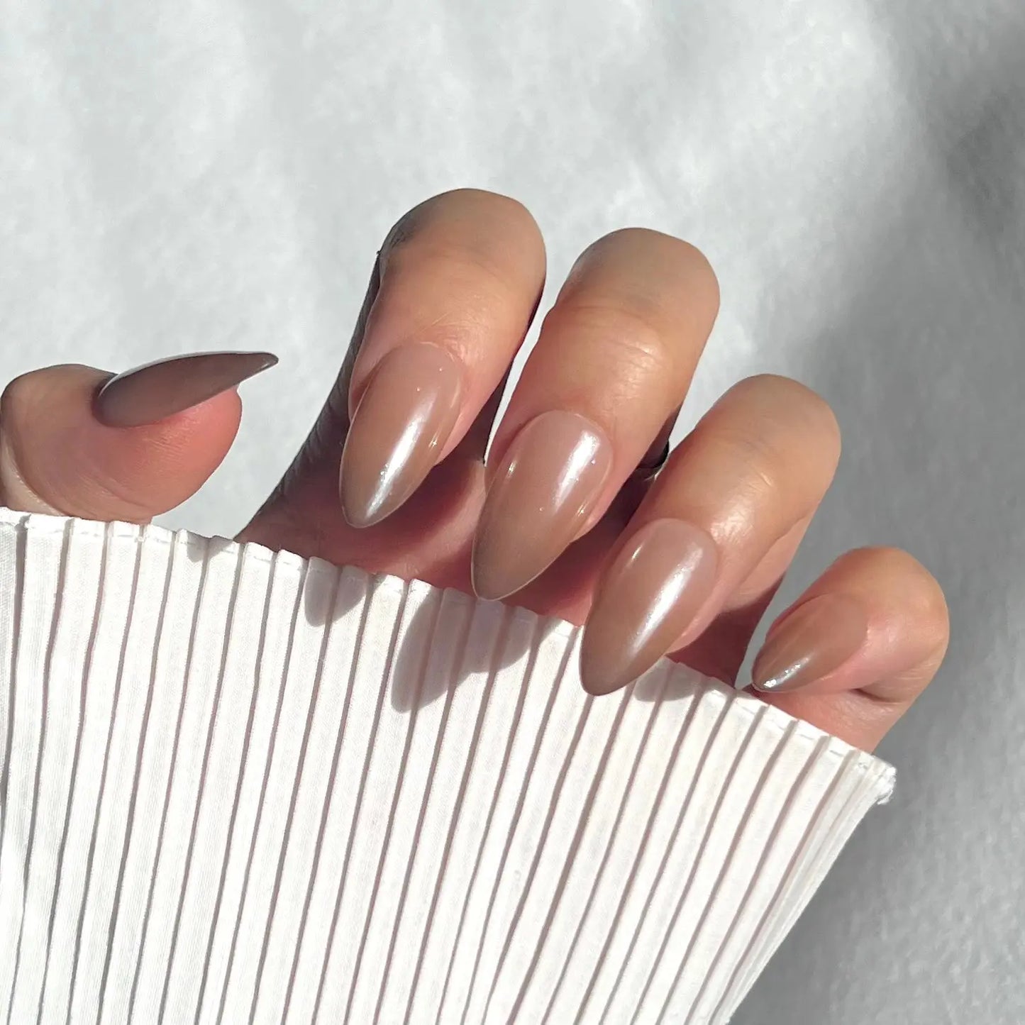  A close-up of a hand wearing almond-shaped press-on nails in a translucent beige shade with a smooth, glossy finish, ideal for a natural and sophisticated style.