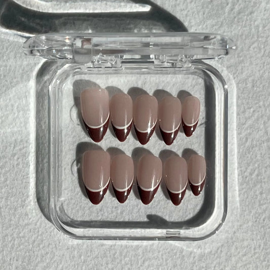 A set of press-on nails displayed in a clear plastic box, featuring a soft nude base with brown tips and a thin white line for a chic and minimalistic look.