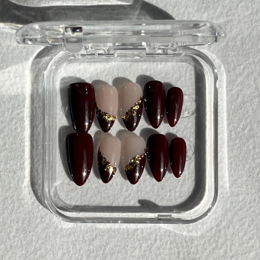 Another view of a hand showcasing the same burgundy and gold leaf-accented press-on nails, elegantly displayed against a soft background.