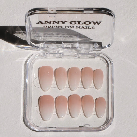 A set of press-on nails displayed in a clear plastic box, featuring a soft peach color with a glossy finish, designed for a simple yet elegant look.