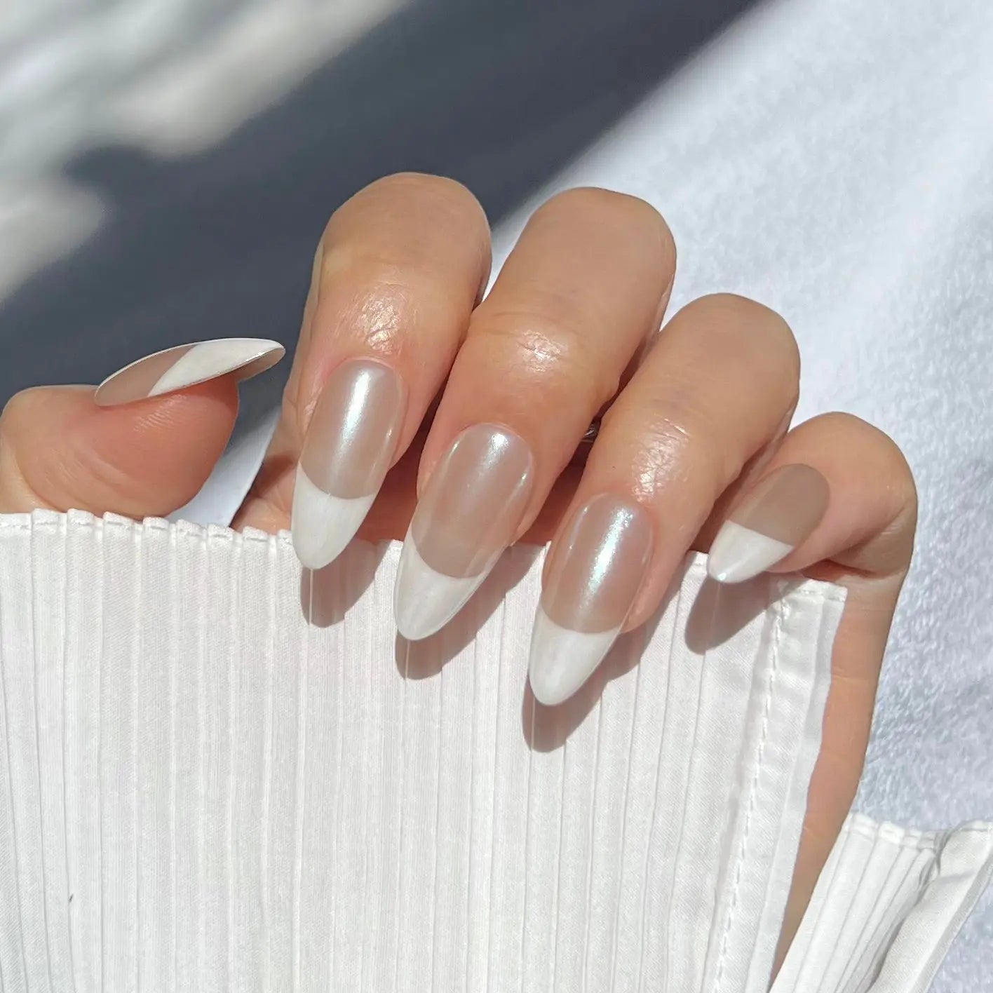 A close-up of a hand wearing press-on nails with pearlescent white tips and a nude base, offering a sophisticated and glossy look.