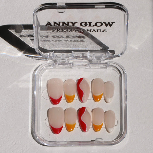 A set of press-on nails displayed in a clear plastic box. The nails have a nude base with different vibrant designs, including some with red tips, others with yellow tips, and a few with a wavy red and white pattern.