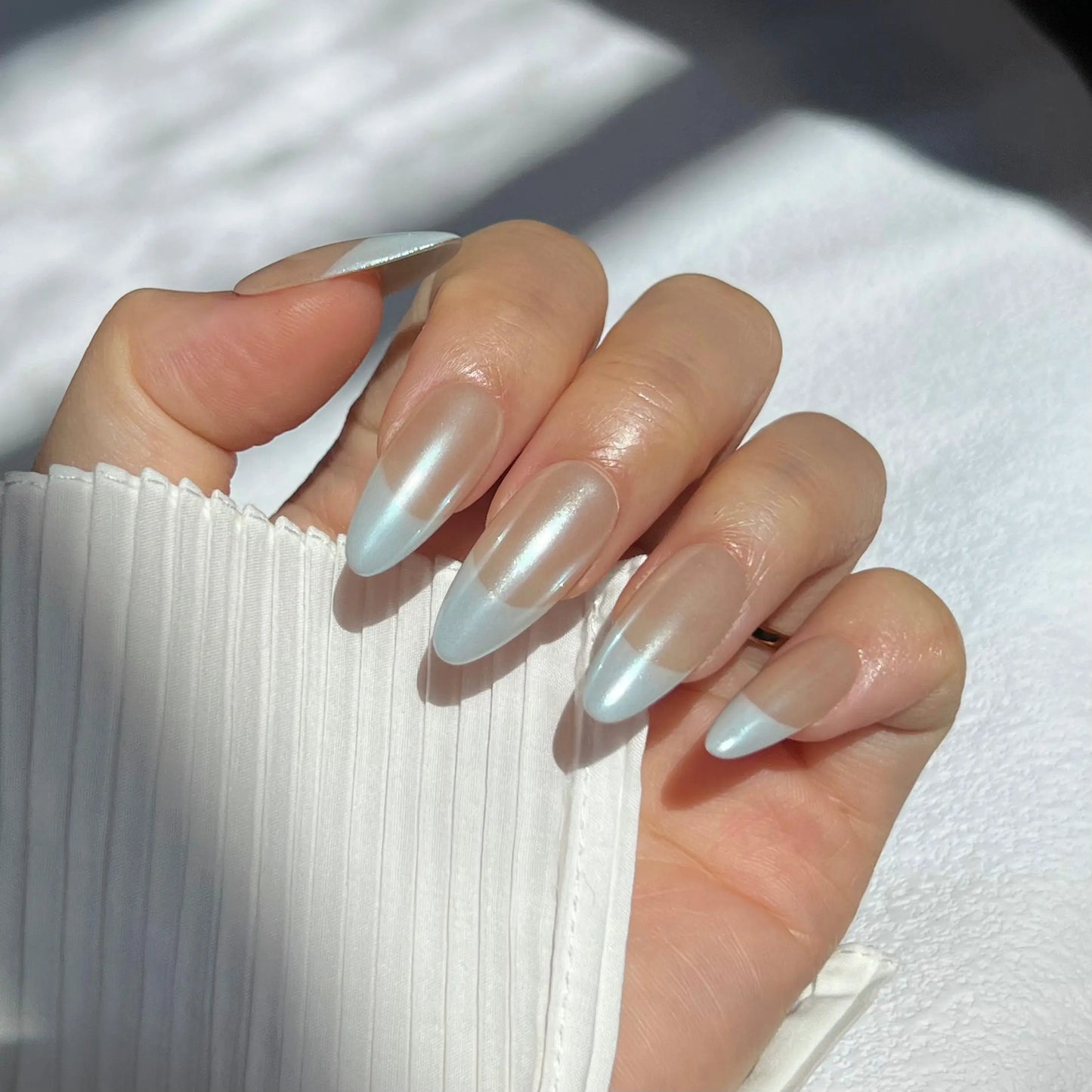  A close-up of a hand wearing press-on nails with soft pastel blue tips and a nude base, offering a simple and elegant look.