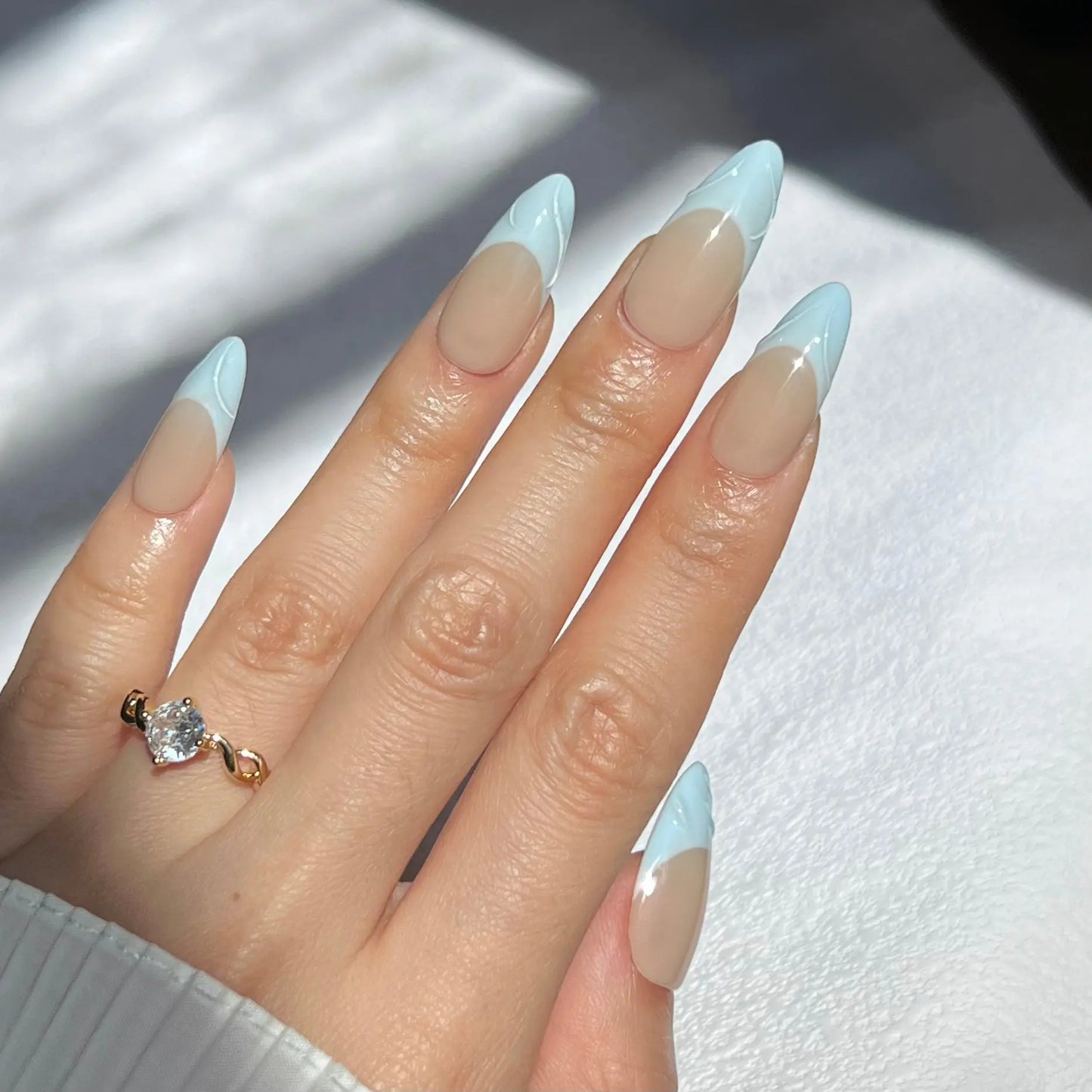 A hand showcasing press-on nails with soft blue wave-like tips and a nude base, creating a refined and tranquil appearance.