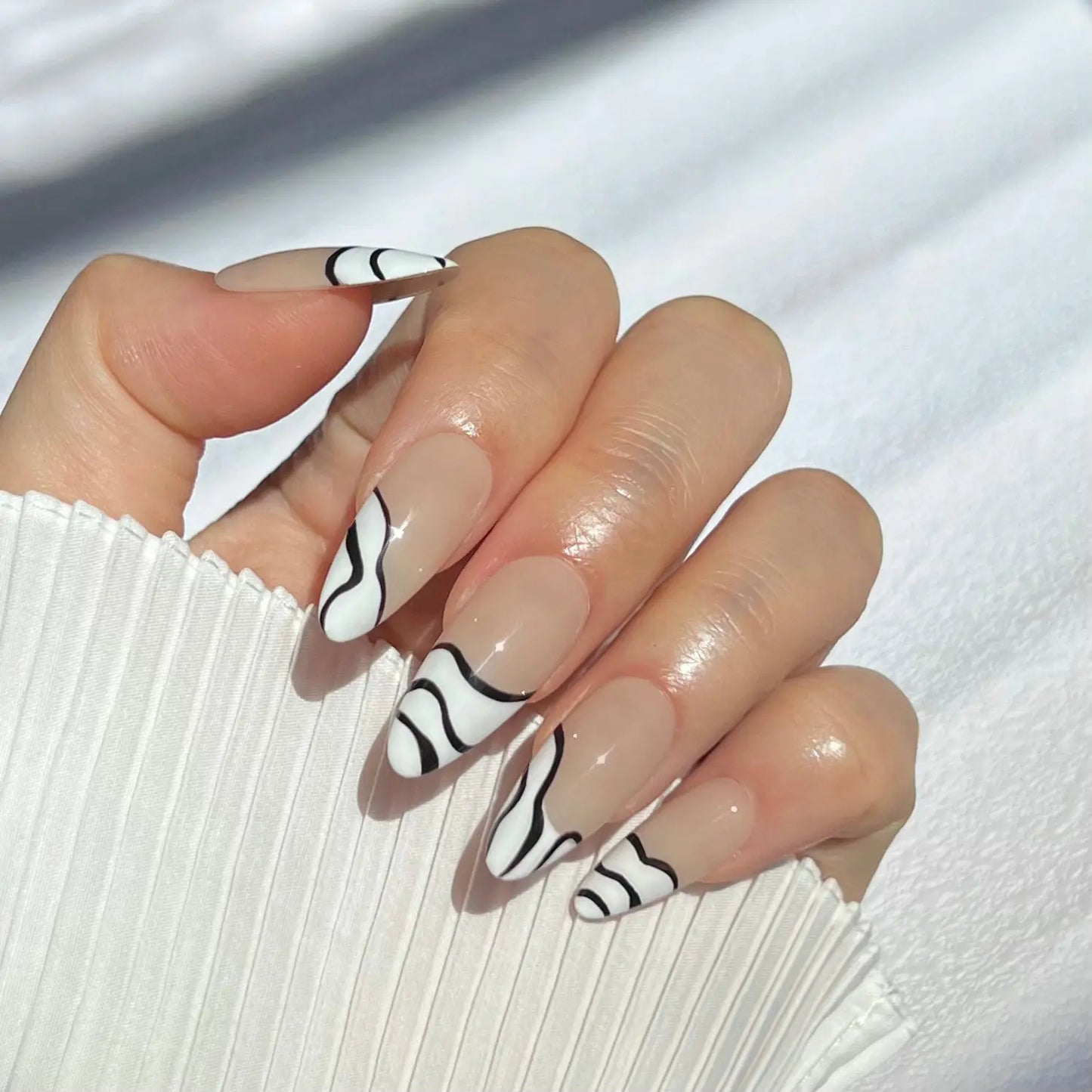 A close-up of a hand wearing almond-shaped press-on nails with a nude base and black and white zebra stripes, perfect for a trendy and bold look.