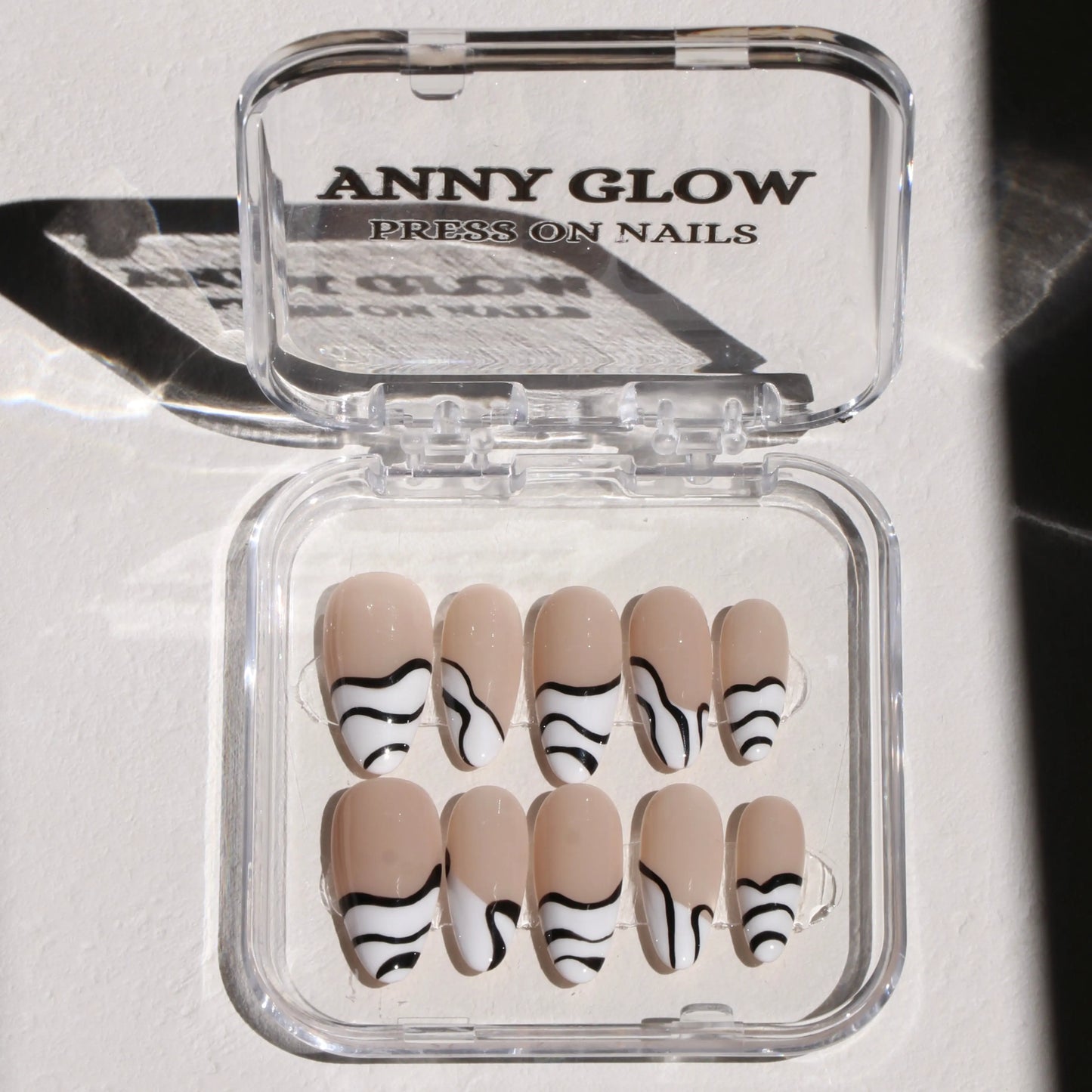 A set of press-on nails in a clear plastic box, featuring a chic nude base with bold black and white zebra stripes, creating a striking and edgy design.